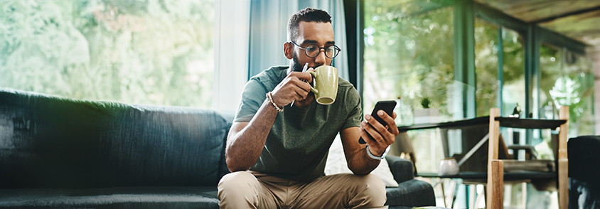 Man drinking coffee while looking at his mobile device.